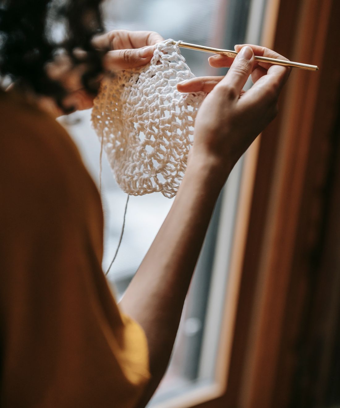 A woman crocheting in a bright, cozy living room with natural window light