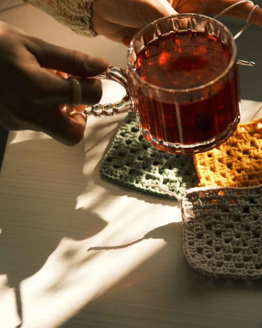 A cream crochet mug rug under a stoneware coffee mug on a wooden table