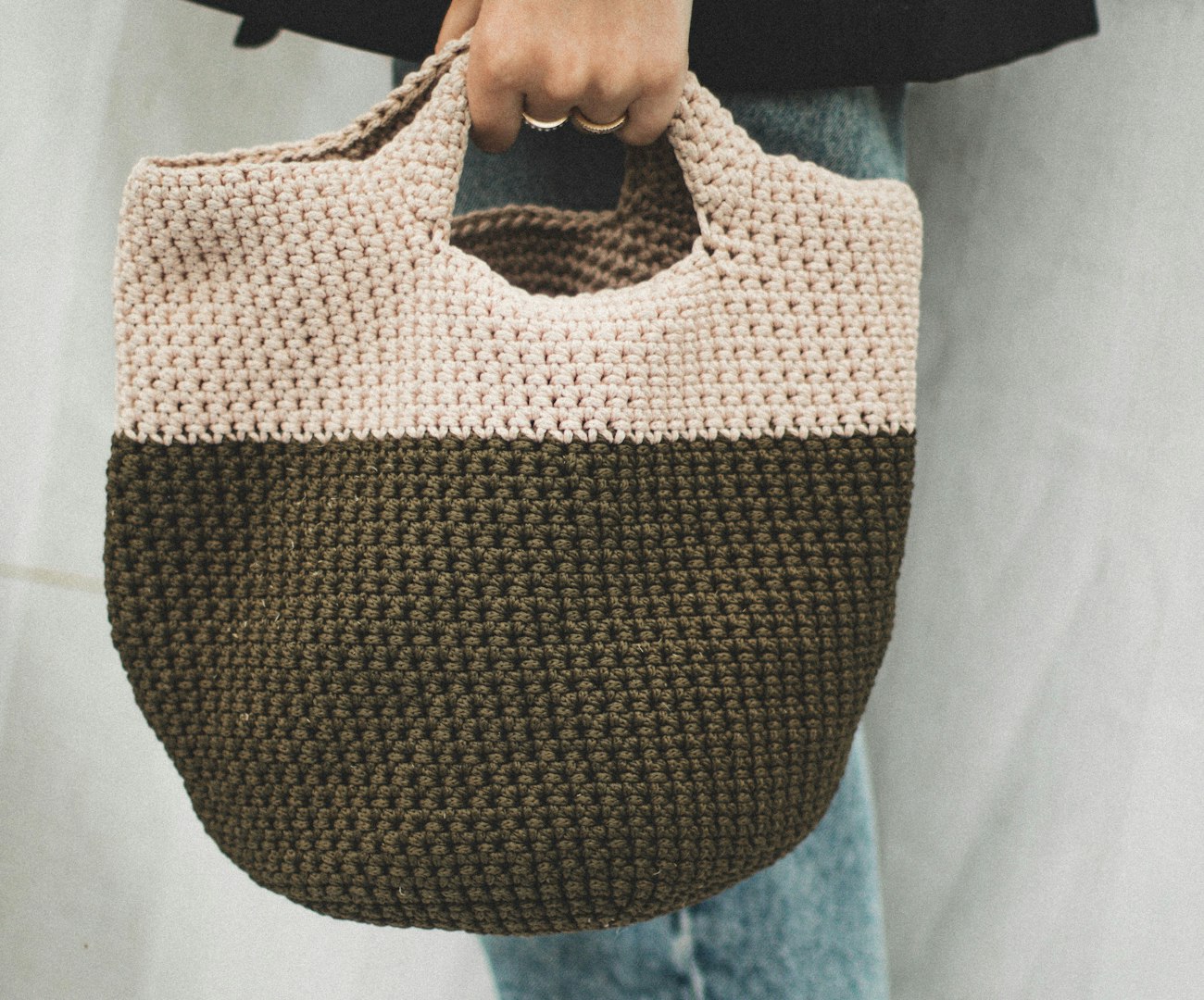 A cream crochet tote bag hanging on a wooden peg rail against a white wall